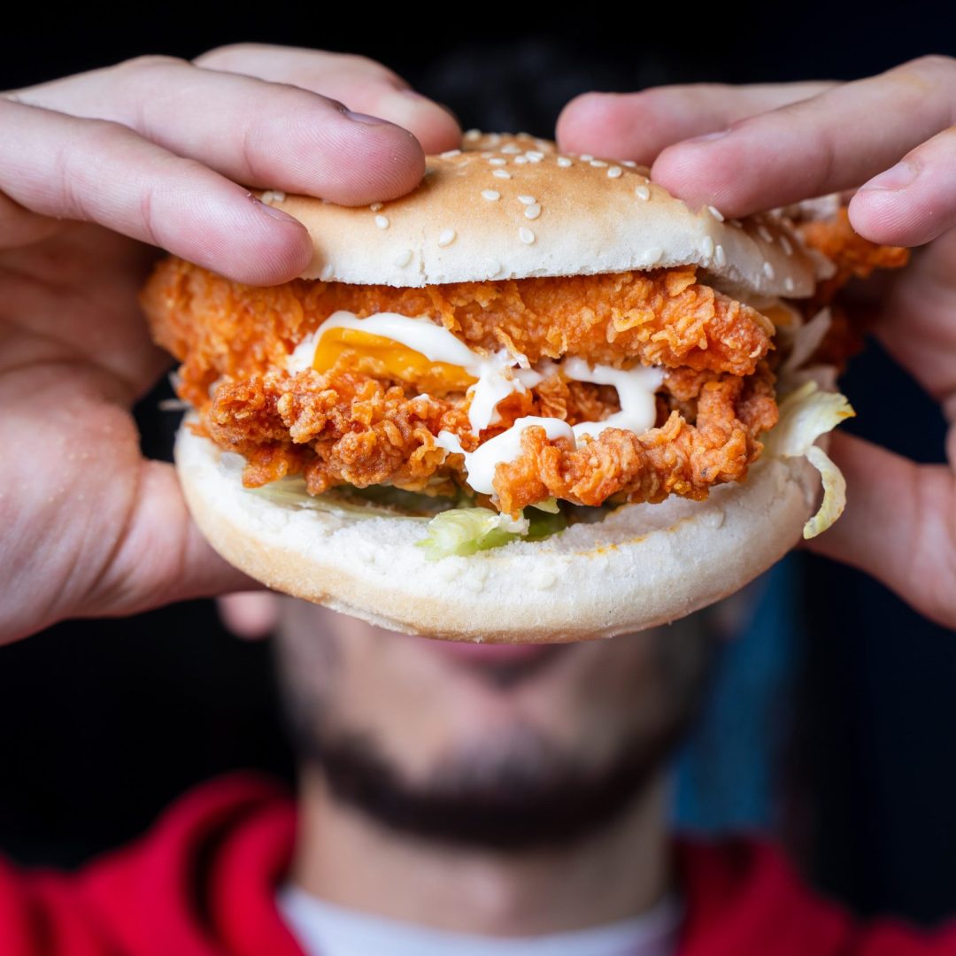 Close-up of a Dixy Chicken burger held in hands, showcasing the crispy chicken and toppings.