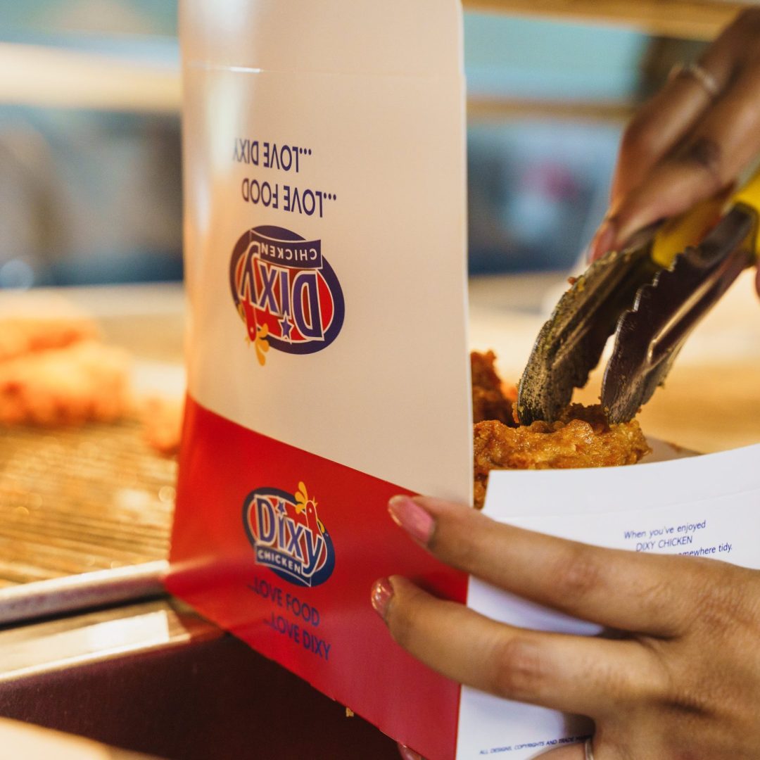Dixy Chicken worker placing crispy fried chicken into a branded takeaway box.